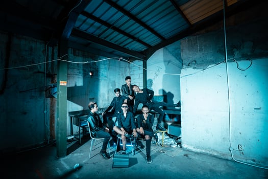 a group of Asian teenagers in black clothes posing very coolly while sitting in a warehouse chair which is lit blue photo