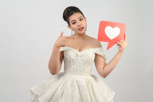 Asian beautiful bride smiling and posing with heart sign on white background photo