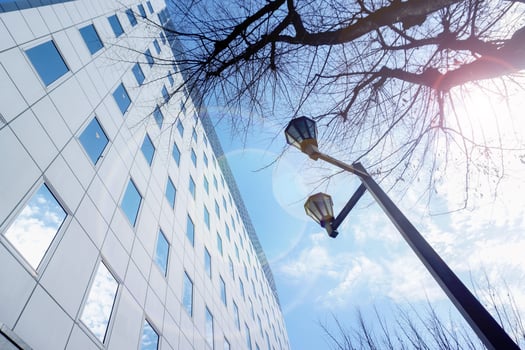 Look up view of office building exterior and silhouette of tree branches and lamp post on bright blue sky and lens flare with sun light background. photo