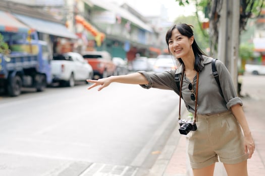 Smiling young Asian woman traveler hitchhiking on a road in the city. Life is a journey concept. photo