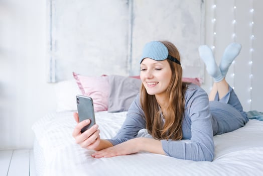 Happy young woman relaxing using and talking with smartphone on bed at home photo