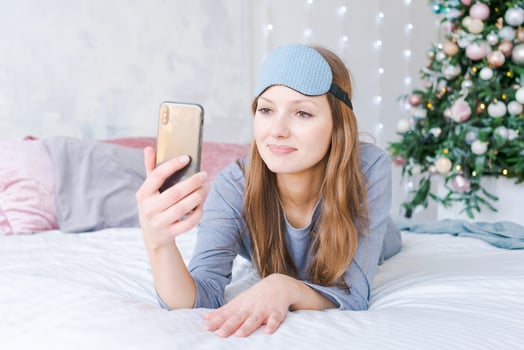 Beautiful young woman looking at phone camera and smiling while lying in bed photo