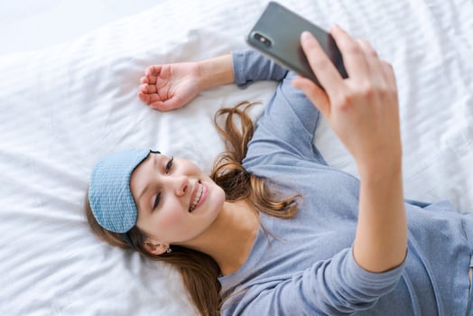 Beautiful woman in blue pajamas looking into phone. Morning starts with phone. photo