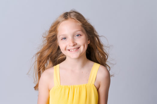 Smiling blonde girl in yellow summer suit posing isolated on light gray photo