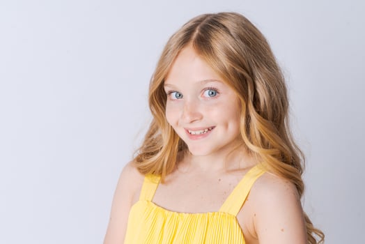 Smiling blonde girl in yellow summer suit posing isolated on light gray photo