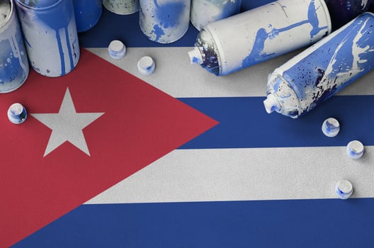 Cuba flag and few used aerosol spray cans for graffiti painting. Street art culture concept photo