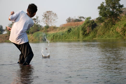 Asian boy is spending his freetimes by diving, swimming, throwing rocks and catching fish in the river happily, hobby and happiness of children concept, in motion. photo
