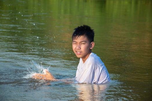 Asian boy is spending his freetimes by diving, swimming, throwing rocks and catching fish in the river happily, hobby and happiness of children concept, in motion. photo