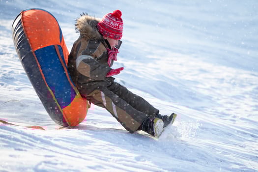 A happy boy up in the air on a tube sledding in the snow.. A boy slides down a hill in winter. photo