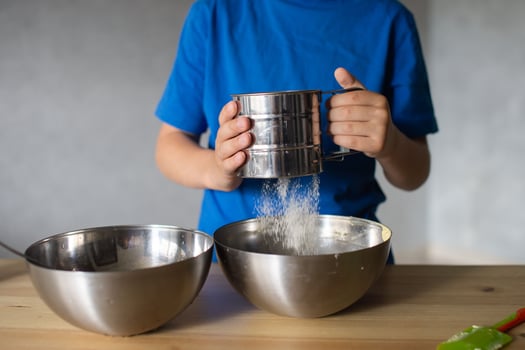 A child prepares dough in metal bowls. Sift the flour. Hands photo