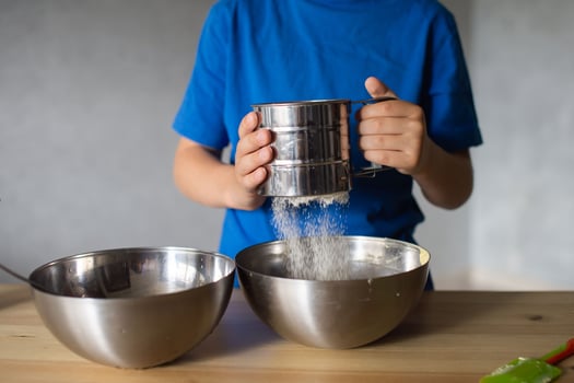 A child prepares dough in metal bowls. Sift the flour. Hands photo