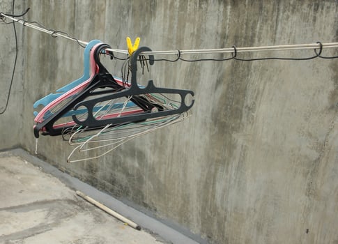 Multiple black, blue, white, and pink clothes hanger on simple thread rope clothes line isolated photo on gray concrete walls and flooring at roof top.