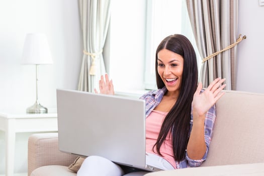 Attractive happy young woman sitting on the sofa using laptop computer, having video chat, waving, talks with her friend about coronavirus and stay home during online video call. Working home photo