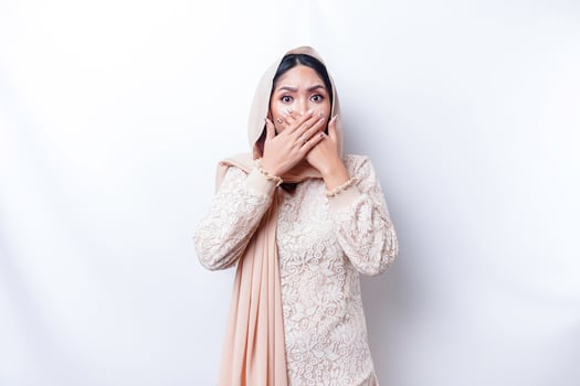 Oops Surprised young Asian Muslim woman covering mouth with hands and staring at camera while standing against white background photo