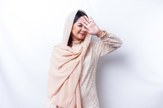Young Asian Muslim woman isolated on white background, looks depressed, face covered by arms frightened and nervous. photo