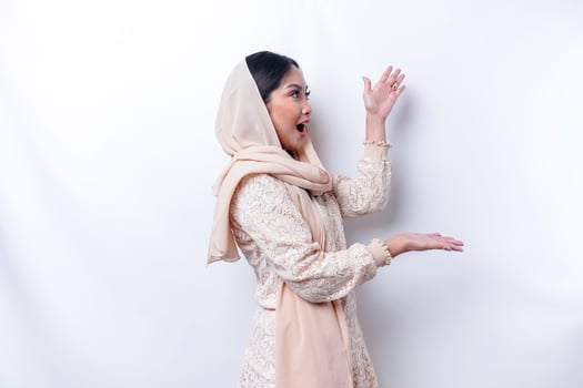 Shocked Asian Muslim woman pointing at the copy space on beside her, isolated by white background photo