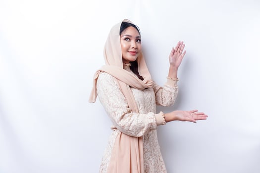 Young Asian Muslim woman smiling while pointing to copy space beside her photo