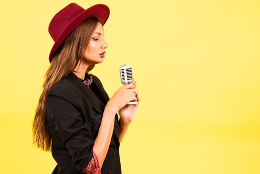girl in a black suit on a yellow background sings in a retro microphone, portrait, music photo