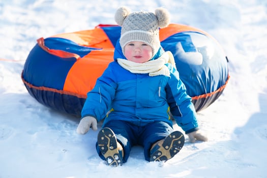 Funny kid in warm clothes sits in the snow with a tubing. photo