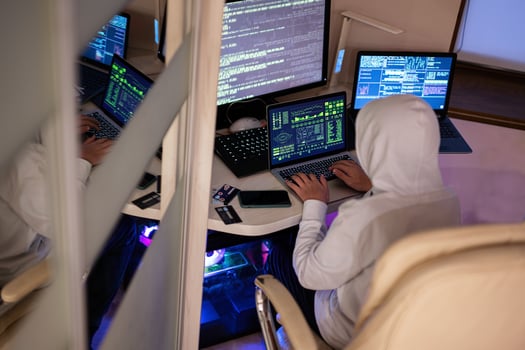 Boy hacker fraudulently use credit card for payment. Internet theft . Man wearing a balaclava and holding a credit card while sat behind a laptop. photo