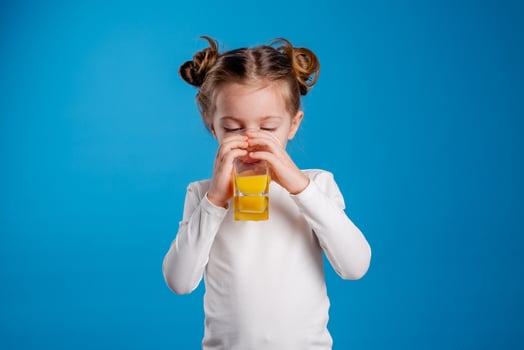 portrait of a little girl of Slavic appearance drinking orange juice on a blue background photo