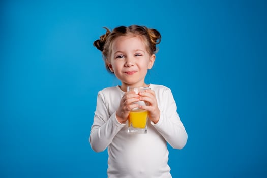 portrait of a little girl of Slavic appearance drinking orange juice on a blue background photo