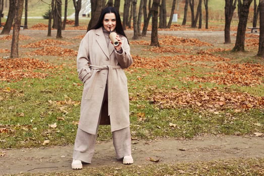 woman in a gray coat walking in the autumn park with a cup of hot drink photo