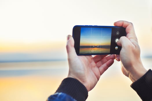 A man taking a photo of the beautiful sunset on his phone