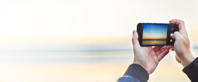 A man taking a photo of the beautiful sunset on his phone