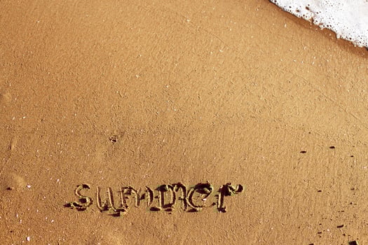 Word summer handwritten on the sandy beach with wave and copy space photo