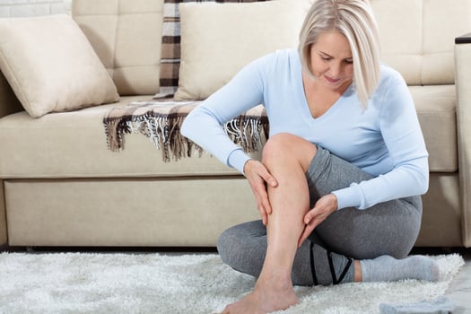 Middle-aged woman suffering from pain in leg at home, closeup. Physical injury concept. photo