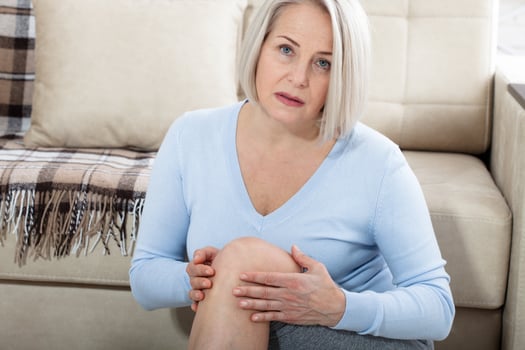 Middle-aged woman suffering from pain in leg at home, closeup. Physical injury concept. photo