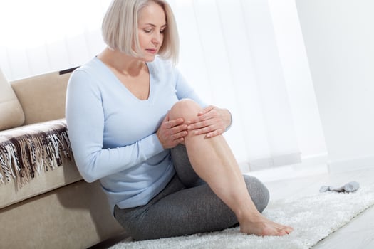 Middle-aged woman suffering from pain in leg at home, closeup. Physical injury concept. photo