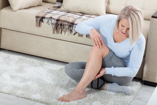 Middle-aged woman suffering from pain in leg at home, closeup. Physical injury concept. photo