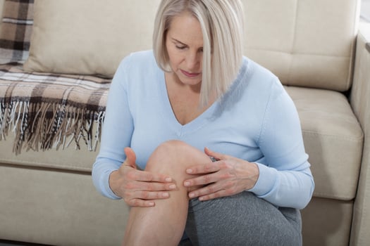 Middle-aged woman suffering from pain in leg at home, closeup. Physical injury concept. photo