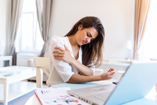 Young woman with hands holding her shoulder pain. Office syndrome and Health care concept. Business woman working with her laptop and with shoulder pain in the home office photo