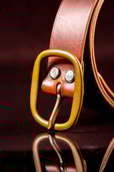 Part of a brown leather belt with a buckle on a dark background. photo