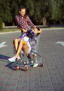 Two happy beautiful teen girls driving shopping cart outdoors photo