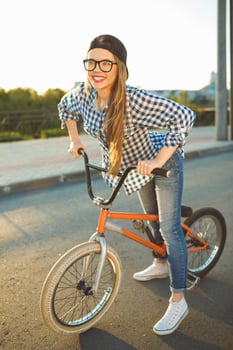 Lovely young woman in a hat riding a bicycle on city background in the sunlight outdoor photo