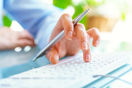 Woman office worker with pen in hand typing on the keyboard photo