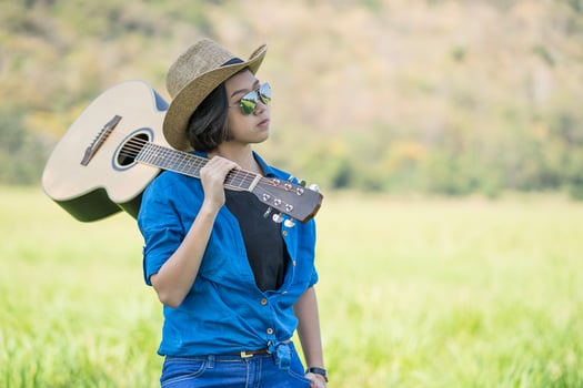 Woman wear hat and carry her guitar in grass field photo