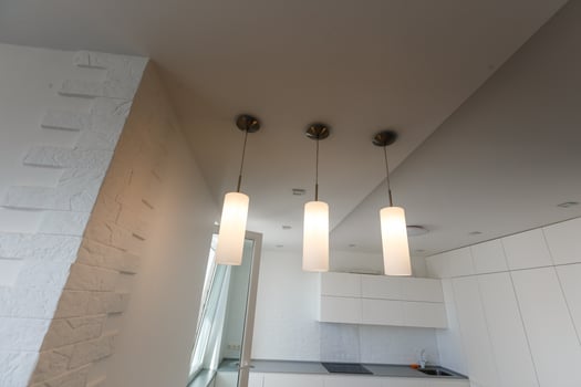 White lamps above kitchen island under a window with bar stools in bright room photo