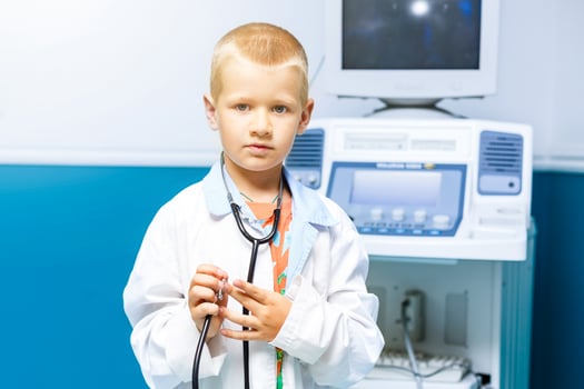 Smiling little boy in medical uniform playing with stethoscope photo