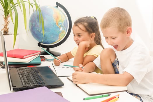 Portrait of two schoolchildren sitting by one desk during drawing lesson while boy looking at his mates copybook photo