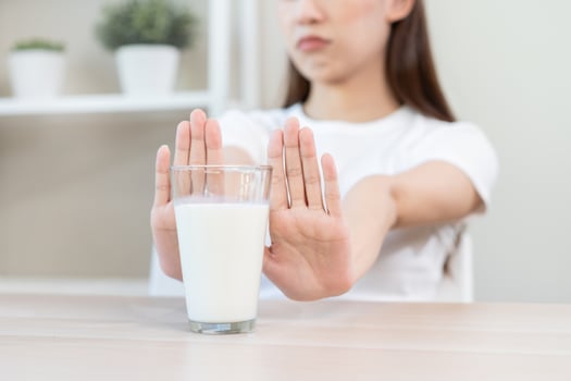 Allergy asian young woman, girl hand in deny, no or push out to avoid for drink milk at home, unhappy and bad stomach ache. Lactose intolerance and dairy food, health problem, belly suffer concept. photo