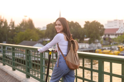 Portrait of young beautiful woman with an electric scooter  over bridge in modern city  background photo