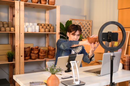 A young Asian man entrepreneur live streaming to sale craft products  to customers in his shop , Technology online business concept. photo
