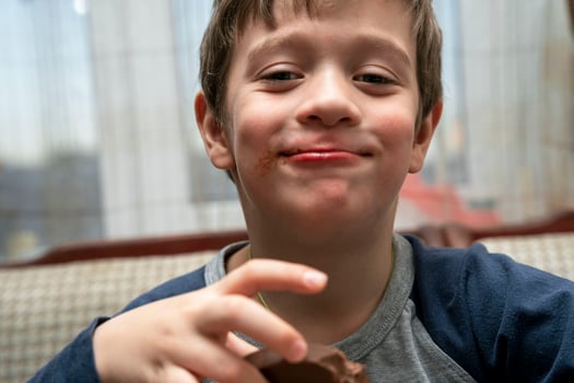 portrait of a funny cute Caucasian boy who eats chocolate sitting at a table in a home kitchen photo