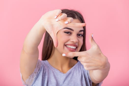 Happy young woman making frame gesture with fingers over pink background. Portrait of a happy smiling woman framing her face with her hands isolated photo