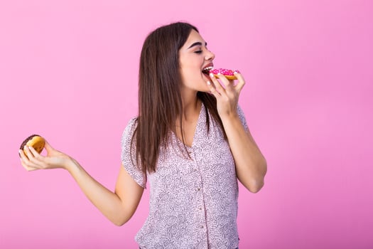 Beauty model girl eating colorful donuts. Funny joyful styled woman choosing sweets on pink background. Diet, dieting concept. Junk food, Slimming, weight loss photo